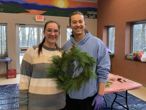 Three people hold a green wreath