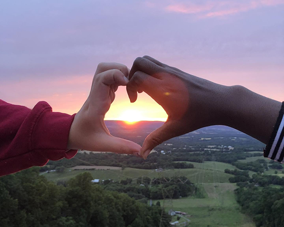 Two hands making a heart with the sunset in background
